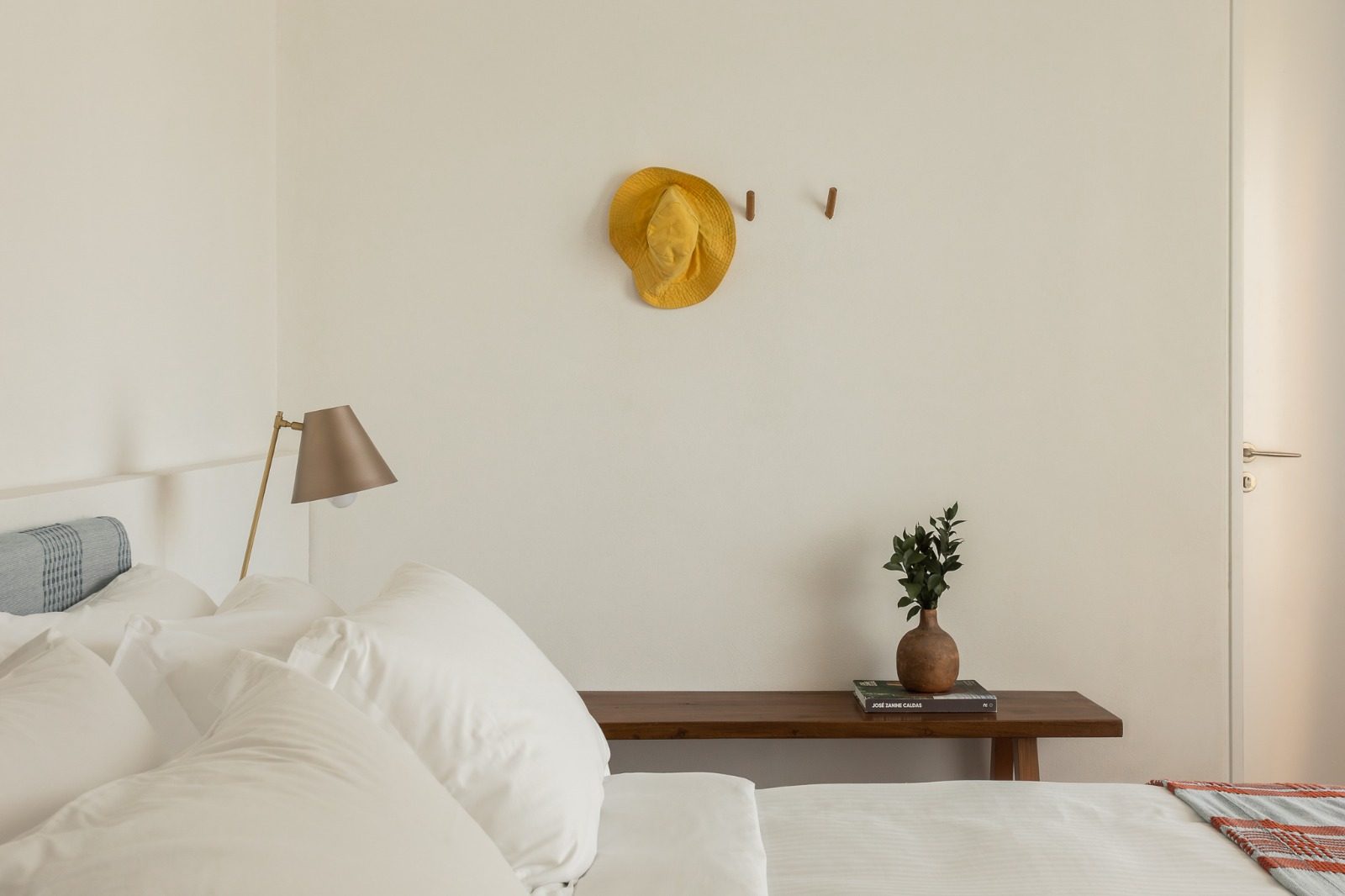 Quarto decorado em tons claros com banco de madeira e vaso de cerâmica